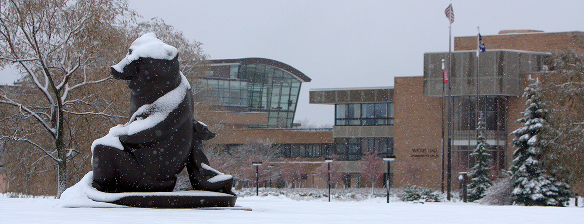 Image of Marshall M. Fredricks' two bears sculpture, covered in snow with SVSU's campus in the background 