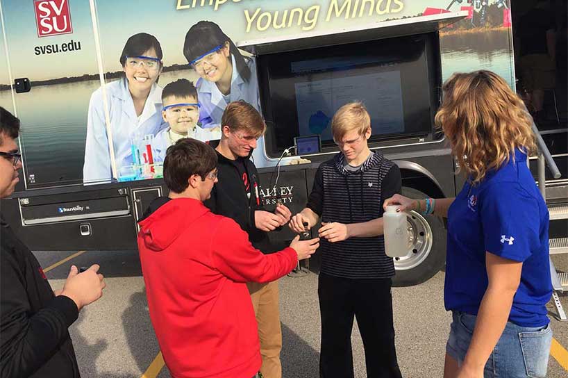 SVSU student assisting high school students with an experiment outside of the STEM mobile bus. 