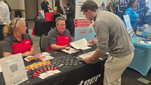 student handing resume to an employer at table during employment fair