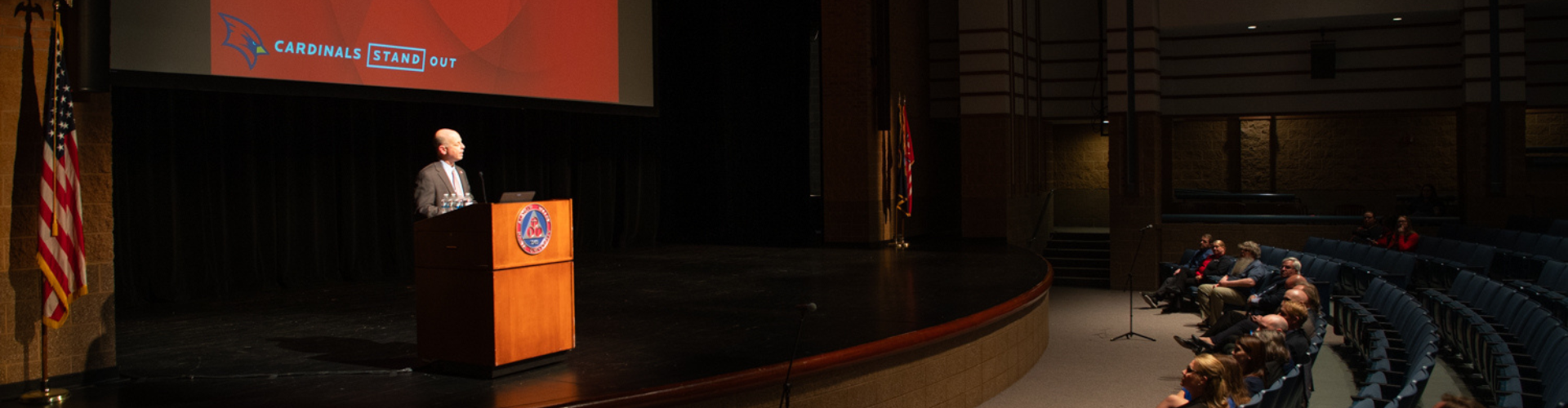speaker at a lectern on a theater stage facing a crowd