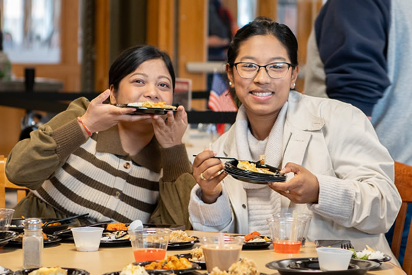 Two SVSU students smile and hold small plates while enjoying food at a campus dining event.