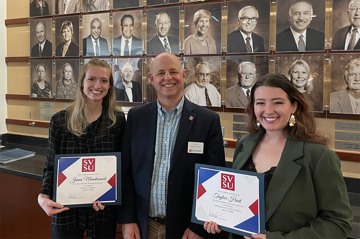 Man in blue jacket flanked by women holding award certificates