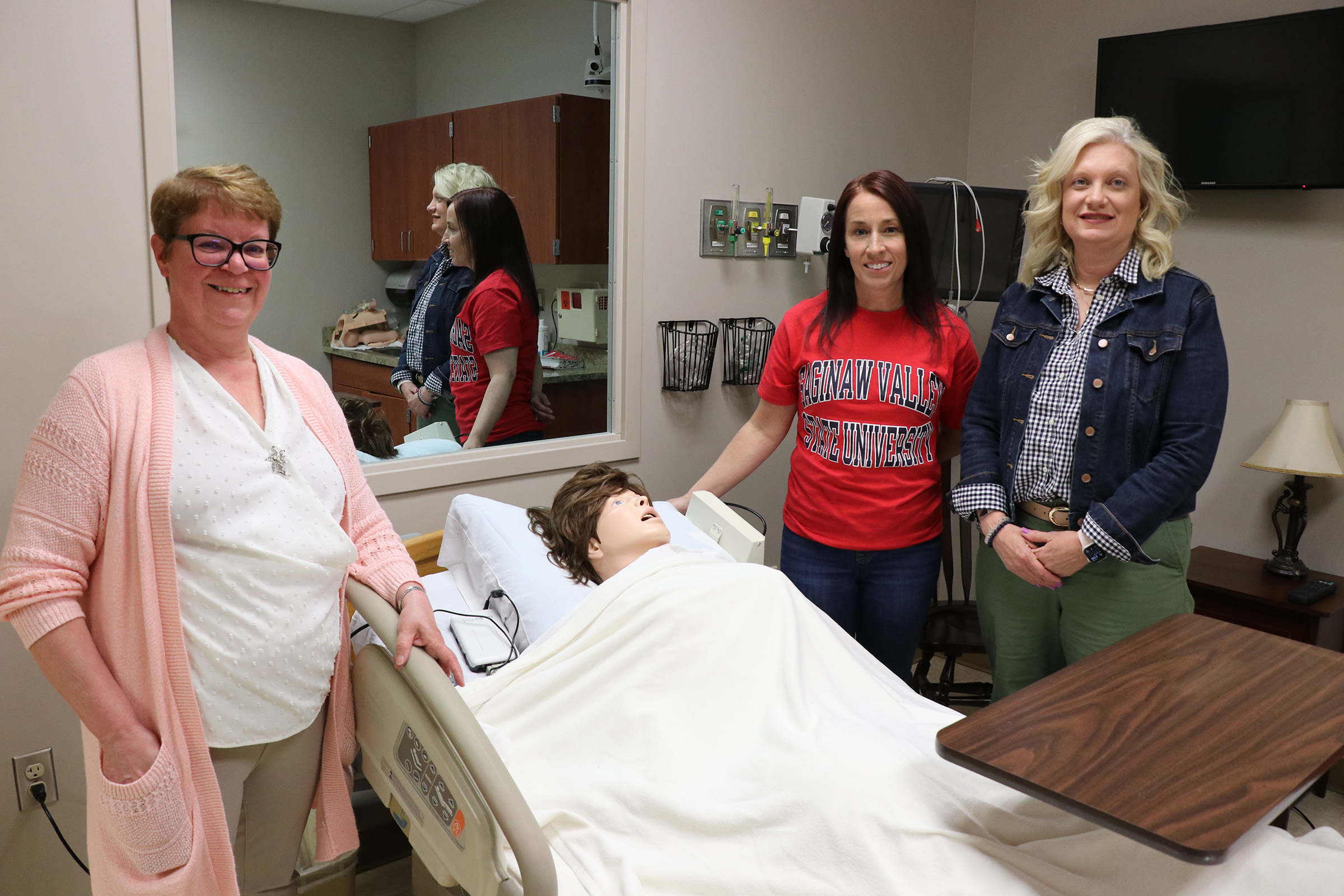 three women standing around hospital bed with patient mannequin
