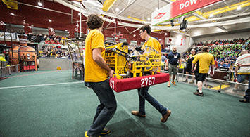 Two students carrying a robot at FIRST Robotics competition.