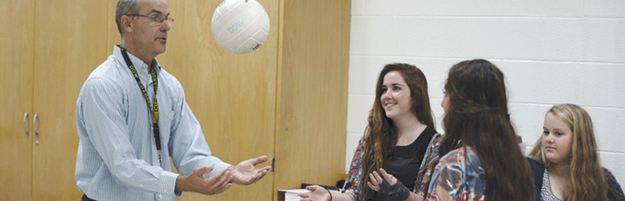 Three students watching a teacher toss a ball in the air.